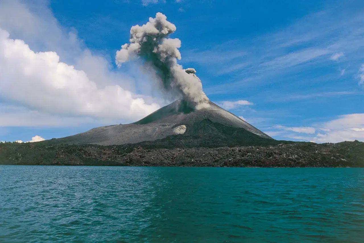 Aktywny wulkan Krakatau wyrzuca kłęby dymu i popiołu na tle błękitnego nieba.