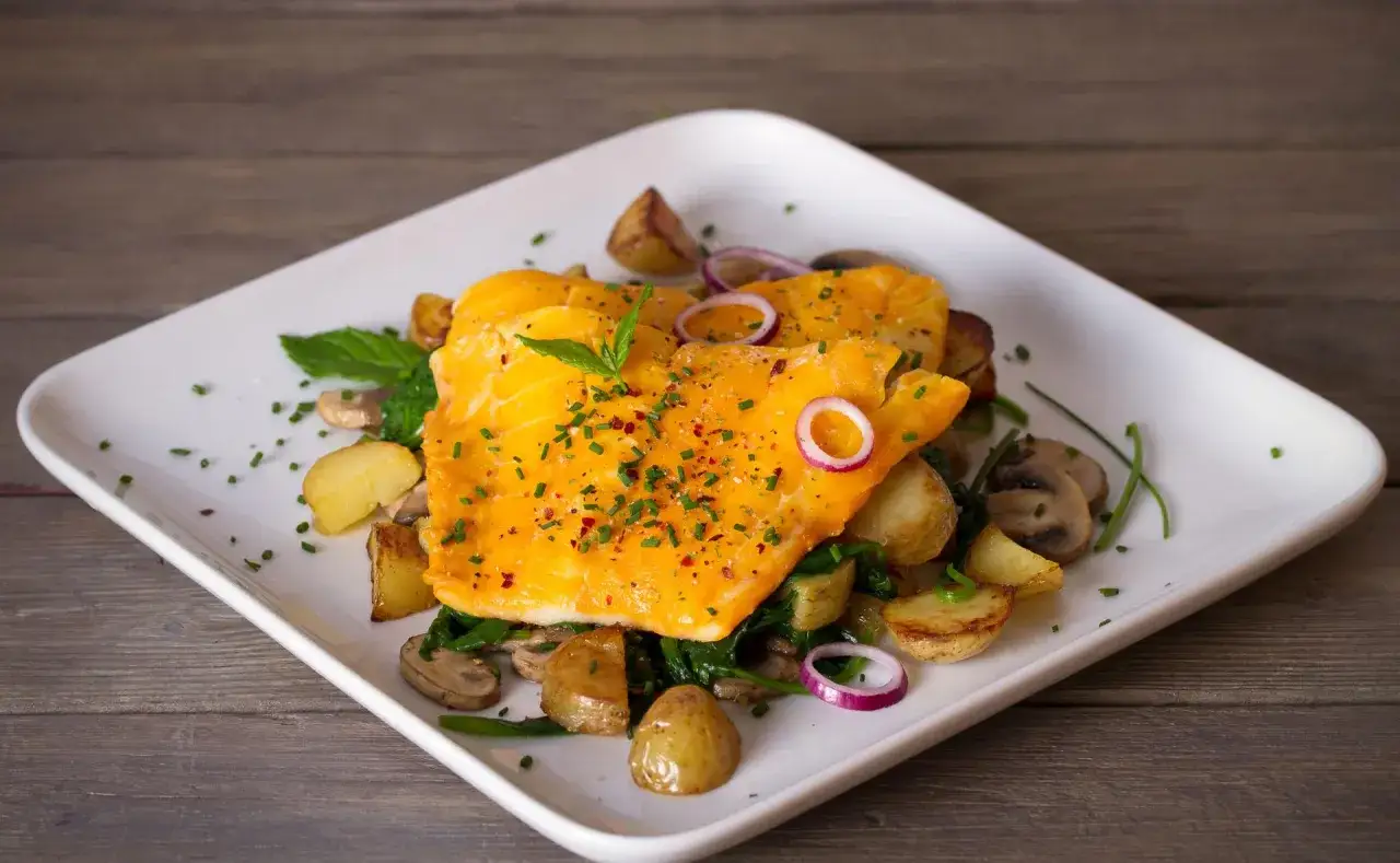 Délicieux haddock cuit, servi avec des pommes de terre rôties, des champignons, des épinards et des oignons rouges. Une assiette colorée et appétissante.