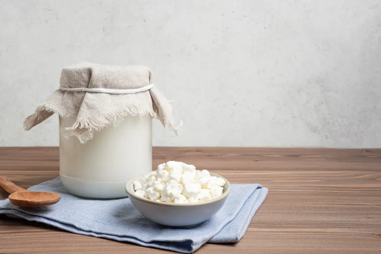 Ein Glas Kefir und eine Schüssel mit Hüttenkäse stehen auf einem Holztisch. Kefir gesund für den Darm.