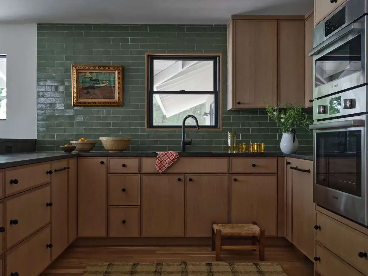 Cuisine noir et bois, mur vert profond. Un tableau nautique ajoute une touche artistique.