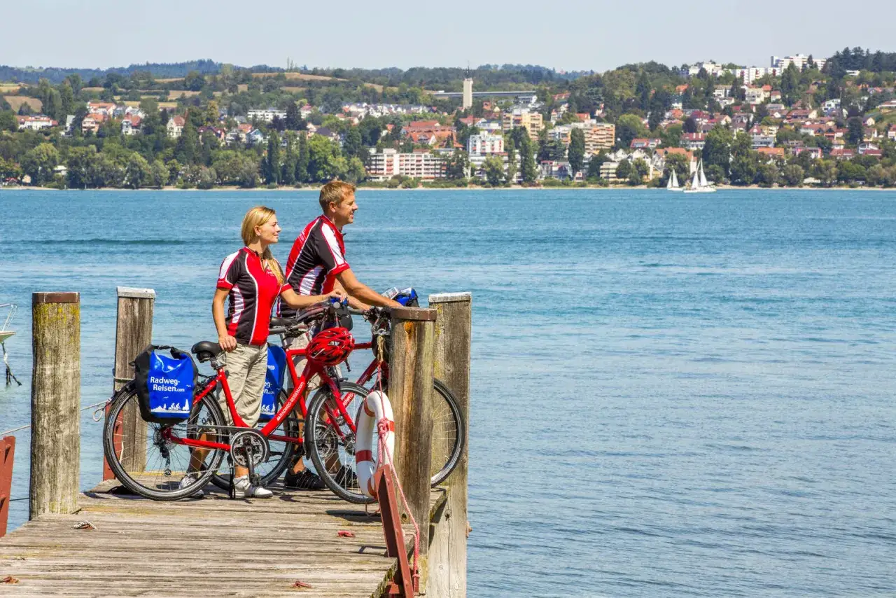 Couple with bikes on a pier, enjoying the view of Lake Constance during their bike tour.