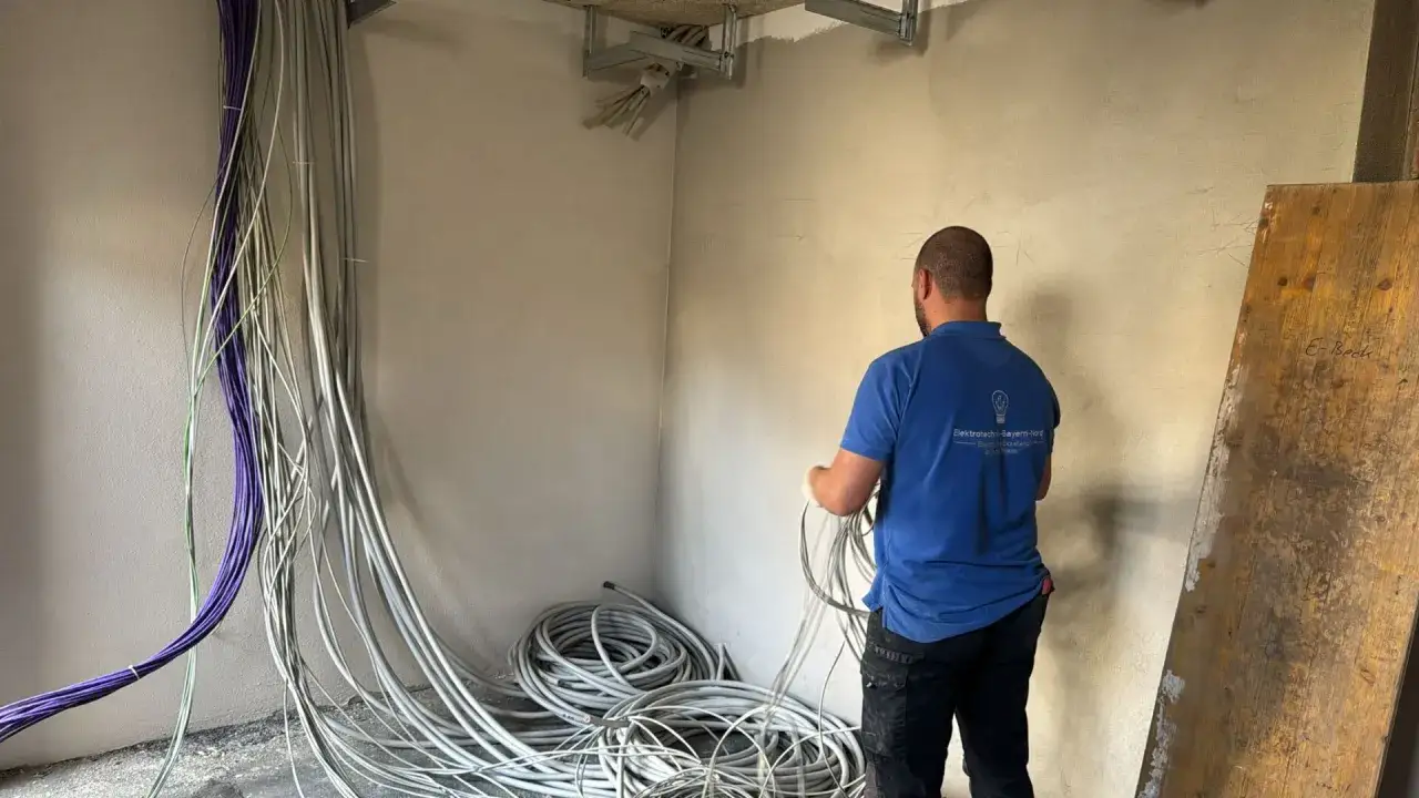 Elektriker bei der Elektroinstallation eines Hauses. Viele Kabel liegen bereit, ein Mann in blauer Arbeitskleidung sortiert sie.