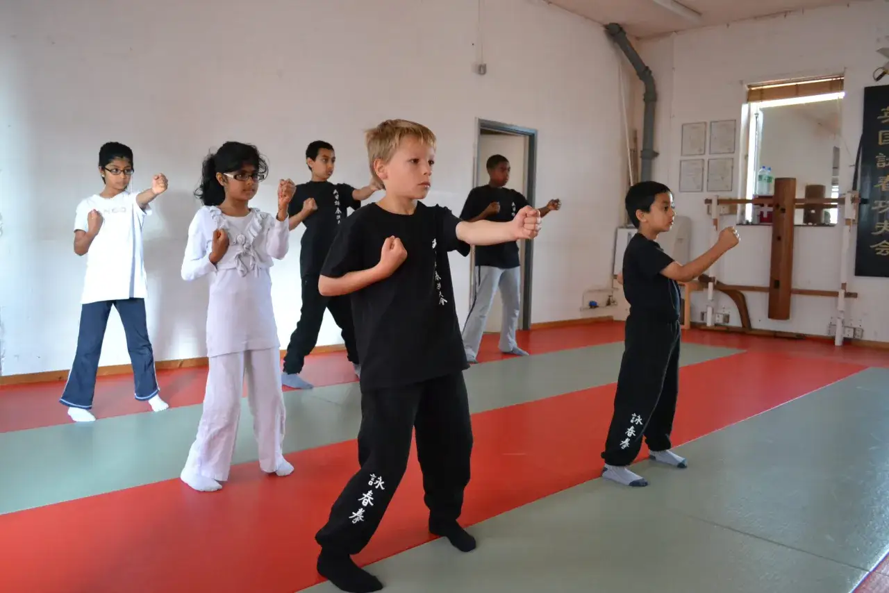 Barn tränar wing chun i en dojo. De står i givakt med knutna nävar.