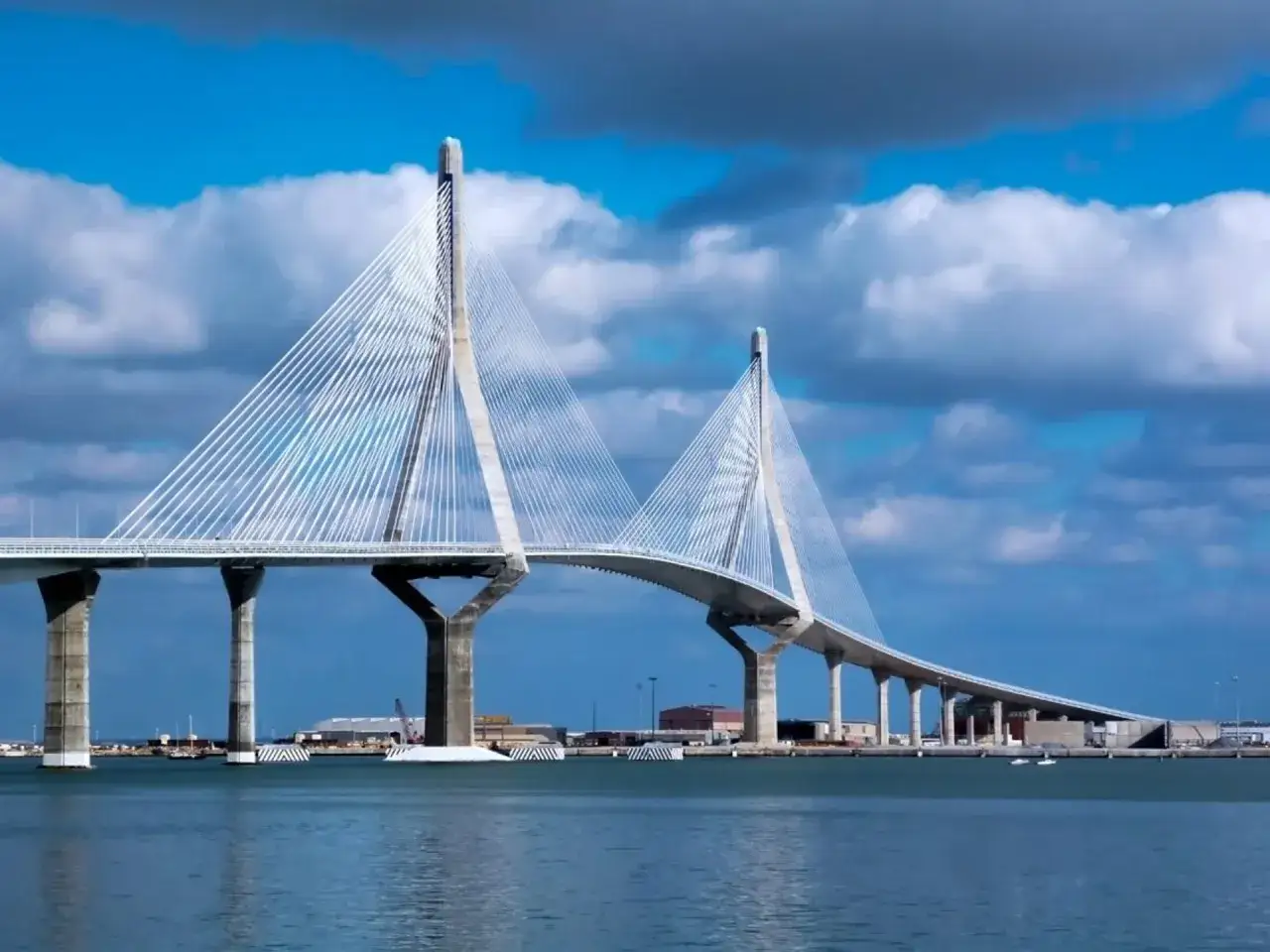 El moderno puente de Cádiz se alza majestuoso sobre el mar azul, con sus cables blancos tensos contra un cielo nublado.