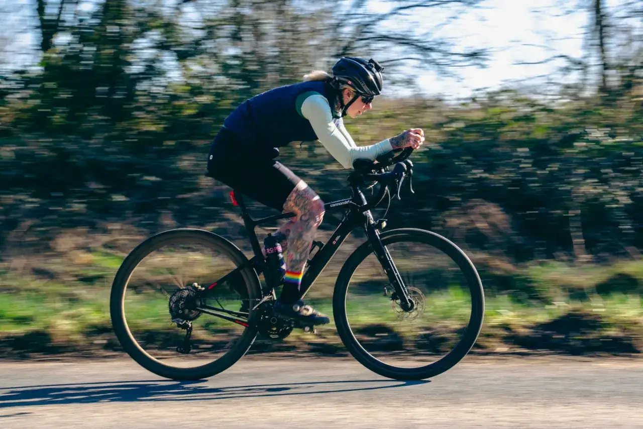 A woman with tattoos rides a black road bike, enjoying the outdoors. This image is perfect for women road bikes for beginners.