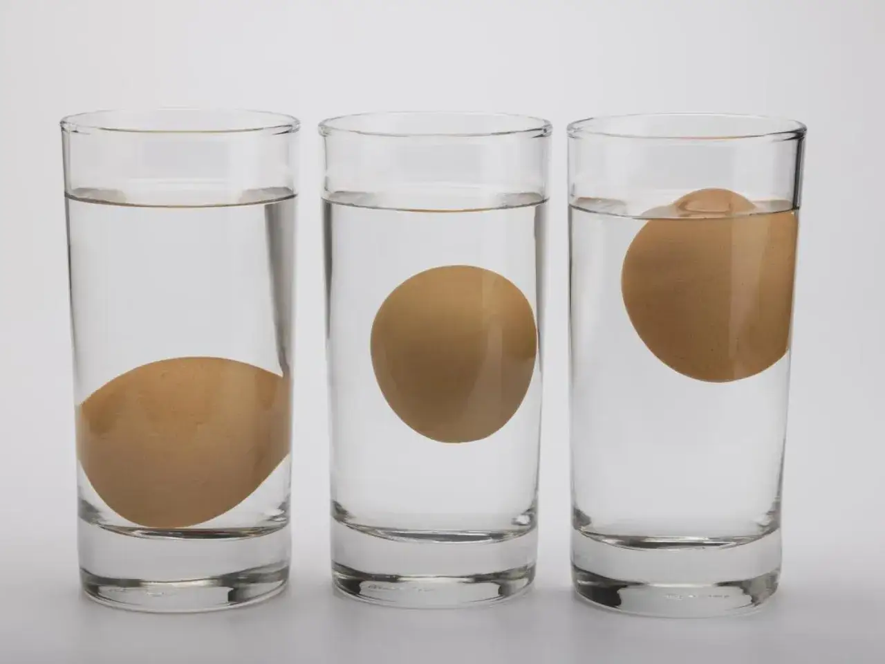 Tres vasos con agua muestran c&oacute;mo saber si un huevo est&aacute; bueno: uno hundido, uno flotando a medias y otro flotando.