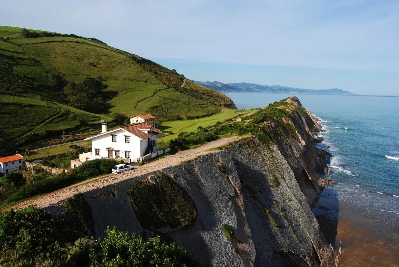 Casas blancas en acantilado verde, ideal para un viaje de **País Vasco en 5 días**. El mar azul y la costa escarpada crean un paisaje impresionante.