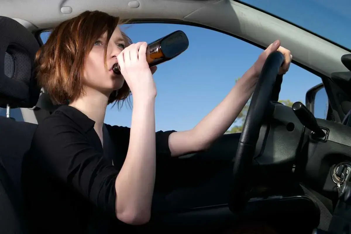 Kobieta za kierownicą pije piwo, zastanawiając się, ile promili alkoholu ma we krwi.