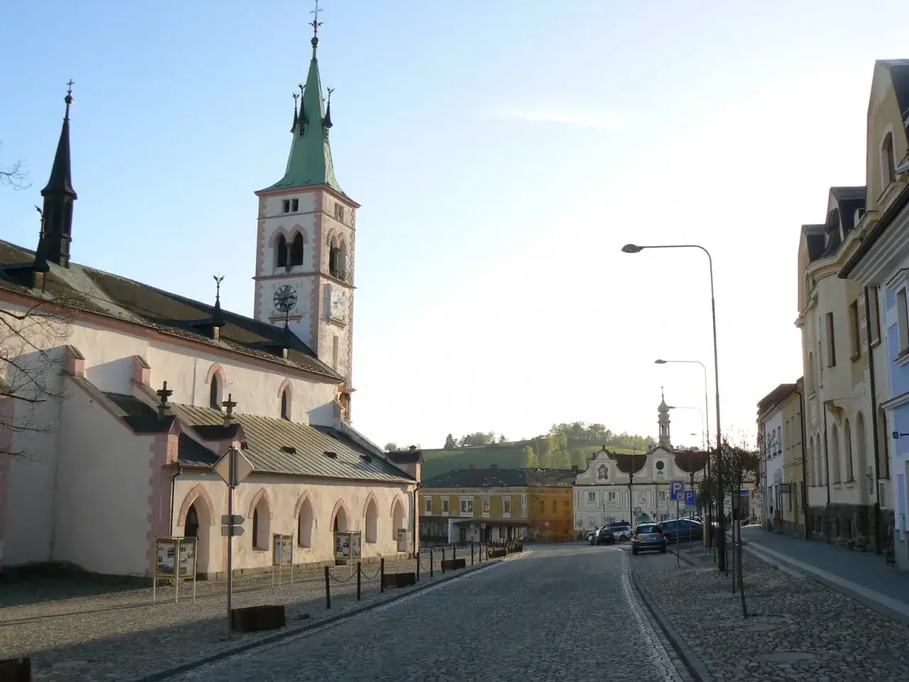 Kopfsteinpflasterstra&szlig;e f&uuml;hrt an einer Kirche mit Kirchturm vorbei in Richtung eines malerischen Platzes in den **Kaspersk&eacute; Hory**.