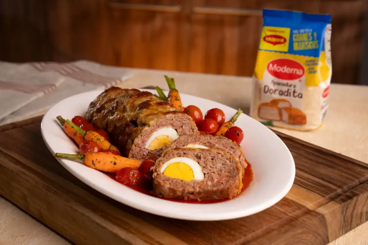 Pastel de carne jugoso con huevo cocido en el centro, acompa&ntilde;ado de zanahorias y tomates.