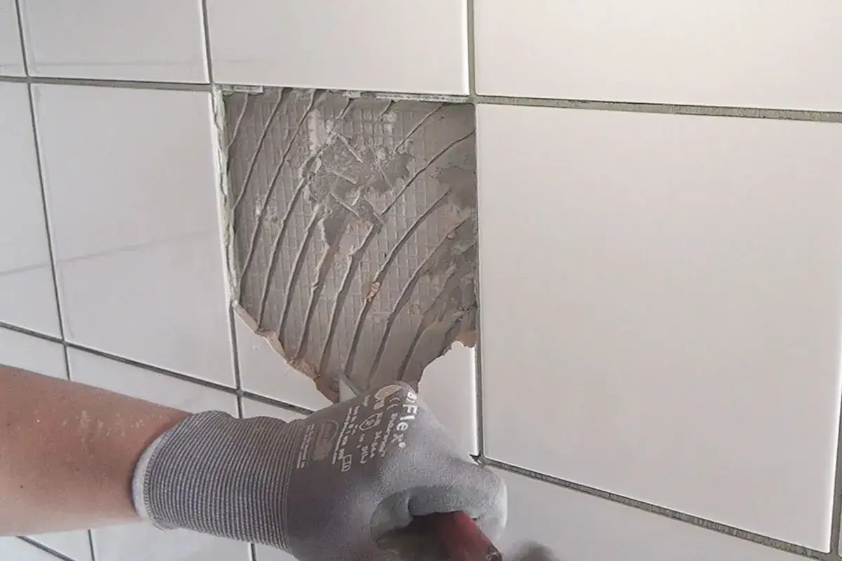 Hand mit Handschuh bereitet vor, um besch&auml;digte Fliesen zu reparieren. Der Kleber ist sichtbar.