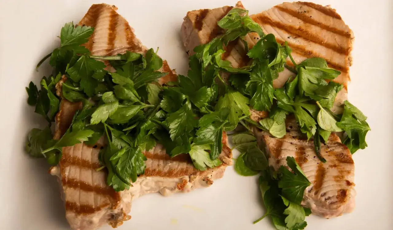 Dos filetes de atún a la plancha, con marcas de parrilla y cubiertos con perejil fresco.