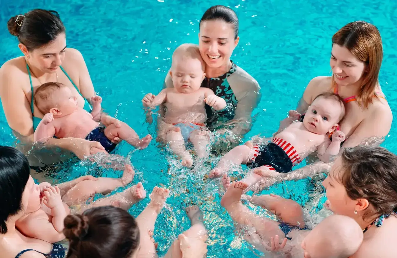 Momenti felici durante un corso di nuoto per neonati in piscina, con bambini e mamme che giocano nell'acqua.
