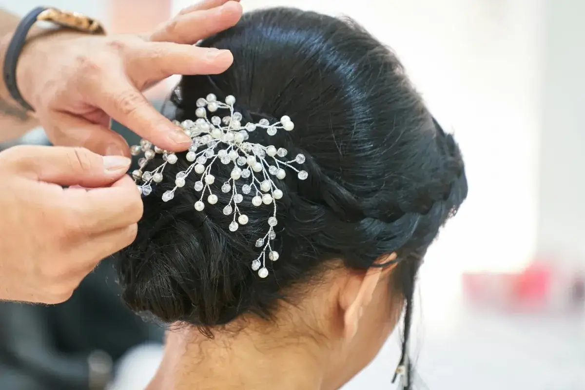 Manos ajustando un tocado de perlas y cristales a un juvenil recogido de boda.