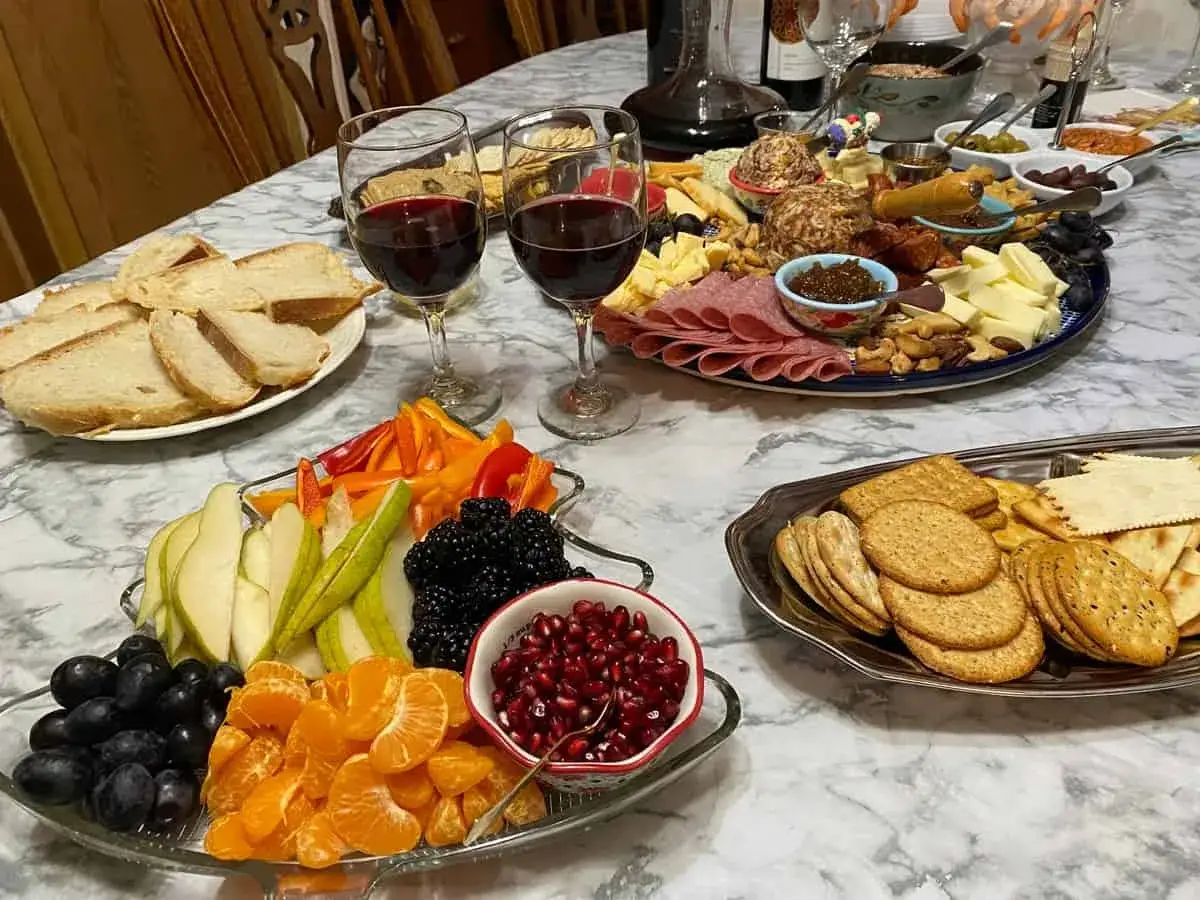 Festliches Buffet mit Käse, Wurst, Brot, Obst und zwei Gläsern fruchtiger Wein.
