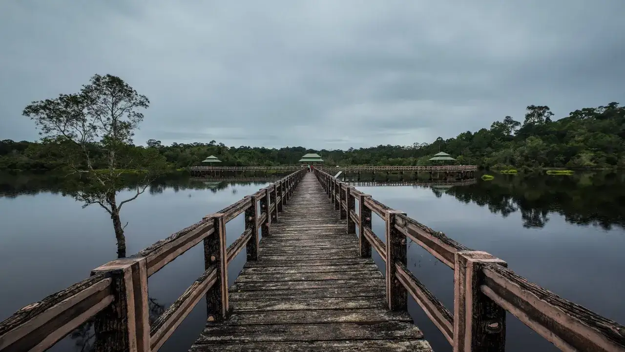 Drewniany pomost prowadzi do altan na spokojnym jeziorze. To malownicza wyspa z Brunei, otoczona bujną zielenią.