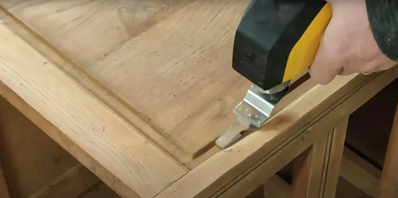 Utilisation d'un outil oscillant pour comment poncer un meuble avec des moulures. La lame s'insère dans les recoins pour un ponçage précis.