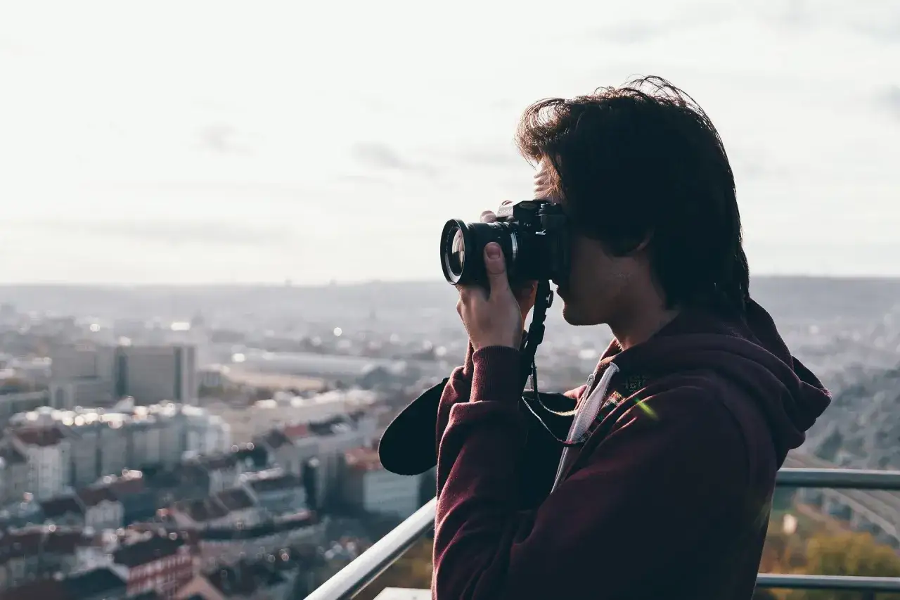 Młody mężczyzna z aparatem fotograficznym na tle miasta. Zastanawia się, ile zarabia fotograf, tworząc piękne ujęcia.