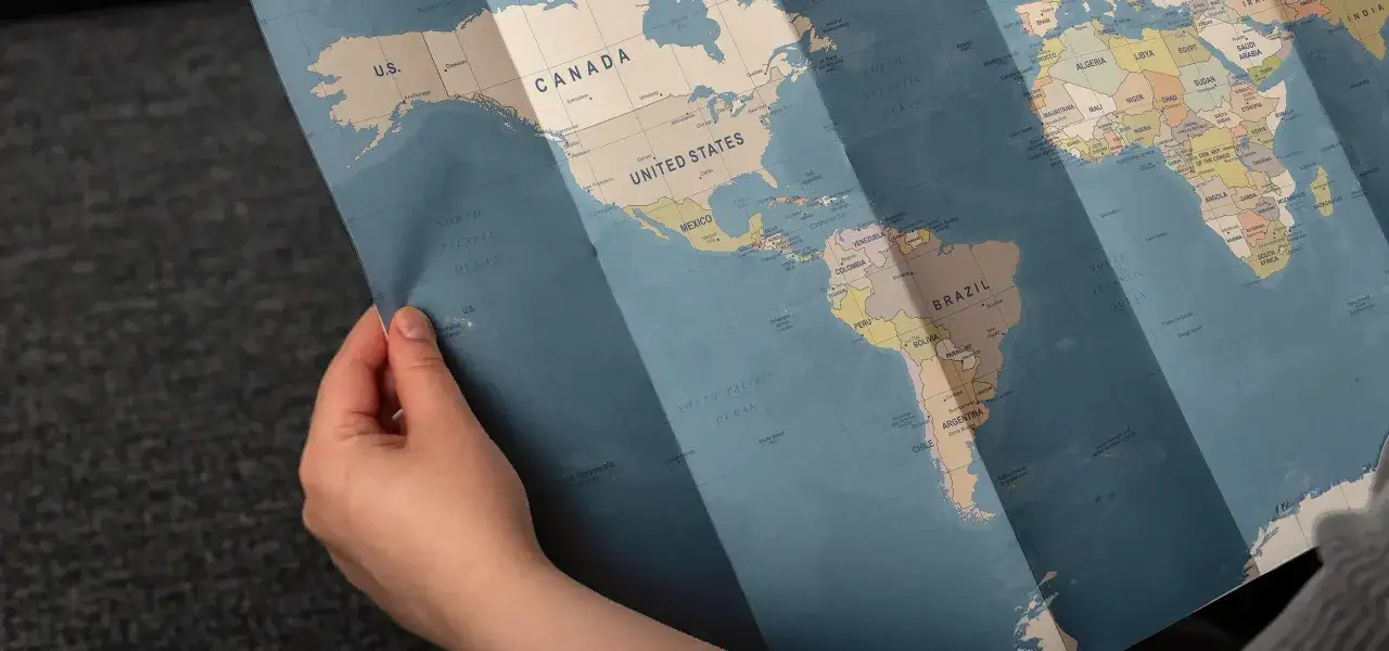 Dłoń trzyma rozłożoną mapę świata, ukazując Amerykę Północną i Południową. To jakby przygotowanie do drukowania map, planowanie podróży.