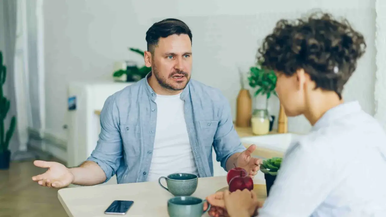 Mężczyzna z niebieskimi oczami, gestykulując, tłumaczy coś kobiecie. Jego ekspresja sugeruje, że chce wywrzeć wrażenie, wykorzystując funkcję impresywną w rozmowie.