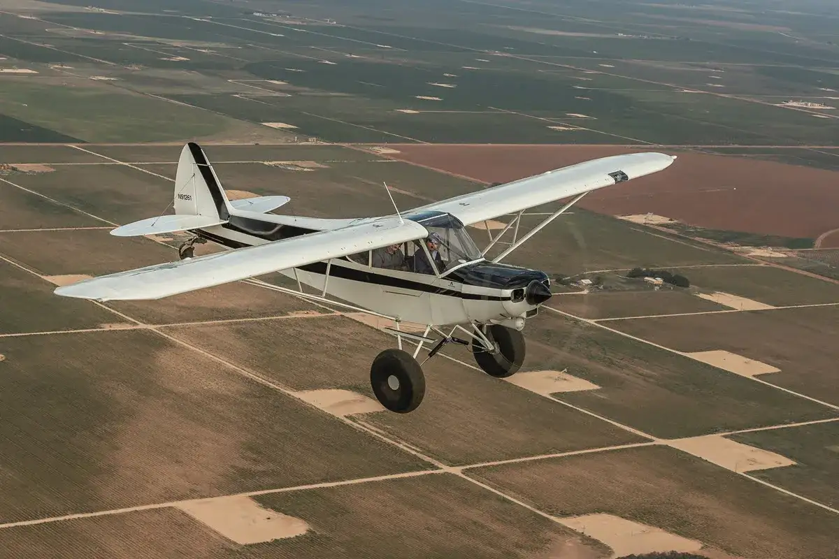 Eine Piper Super Cub fliegt über ein Mosaik aus Feldern.