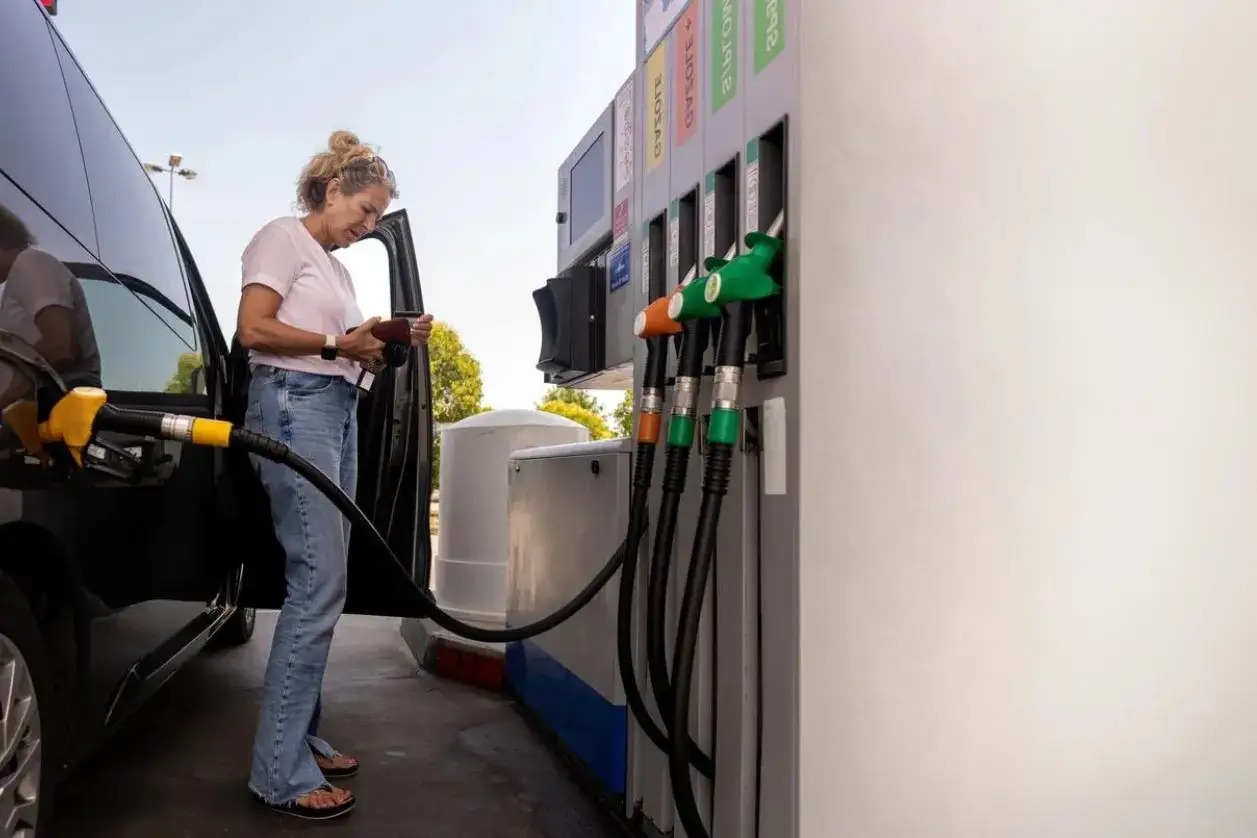 Femme &agrave; la station-service, v&eacute;rifiant sa carte grise pour choisir entre essence ou diesel. Le pistolet de la pompe est pr&ecirc;t.