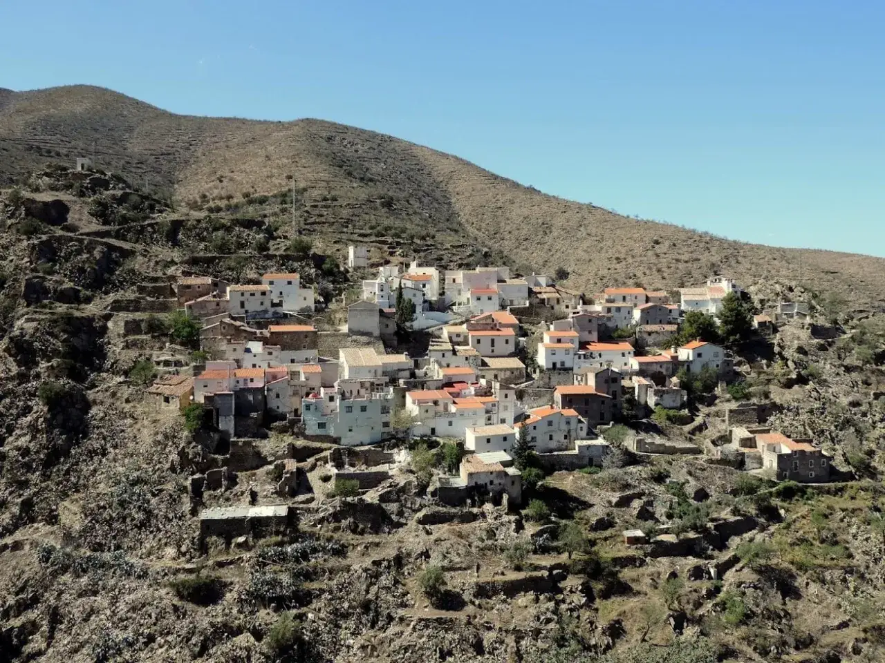 Pueblo blanco de Chercos, Almería, anidado en una ladera árida bajo un cielo azul.