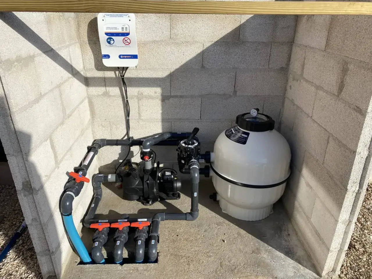 Système de filtration pour piscine en dur : pompe, filtre à sable et coffret électrique installés dans un local technique en parpaings.