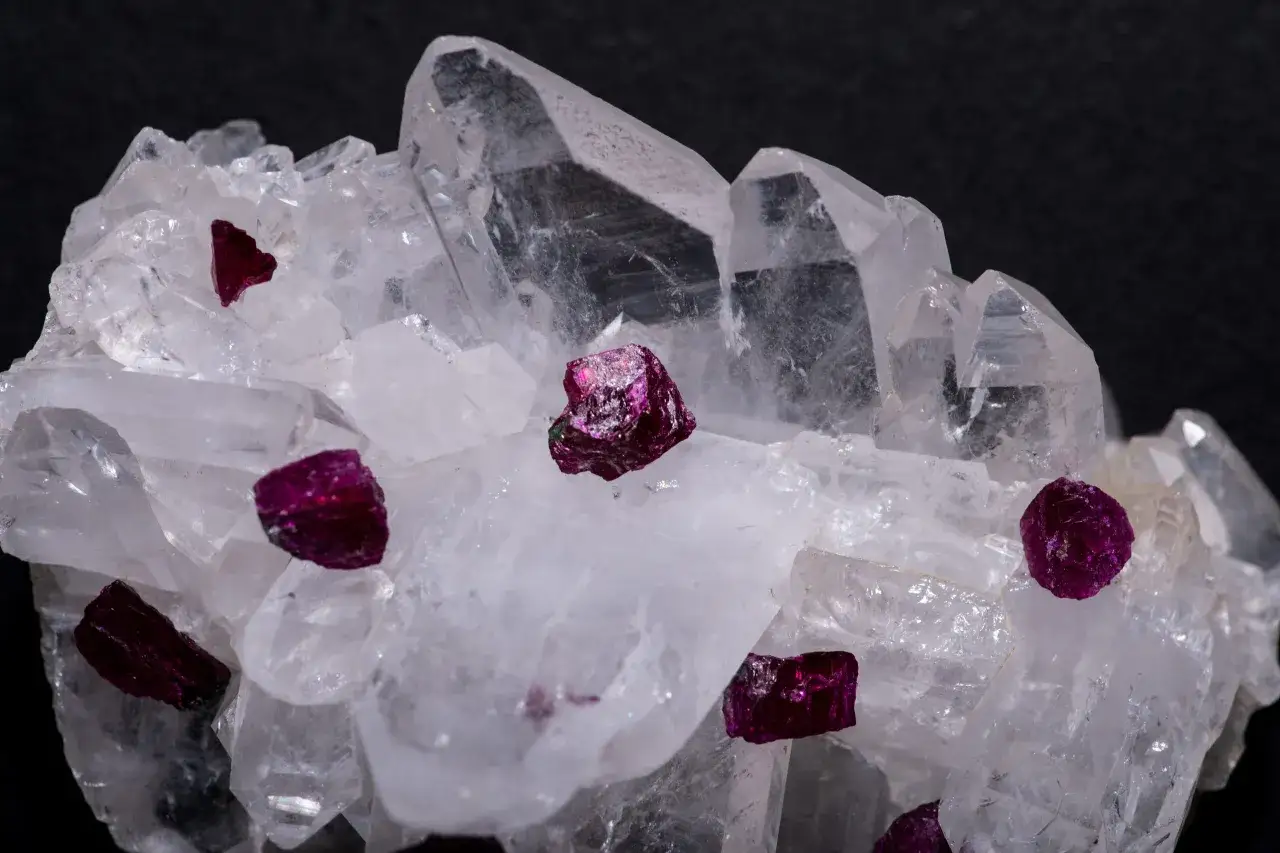 Klarer Quarz mit kleinen, rubinroten Kristallen. Diese Kristalle sind Korund, ein Mineral, das für seine Härte und Schönheit bekannt ist.