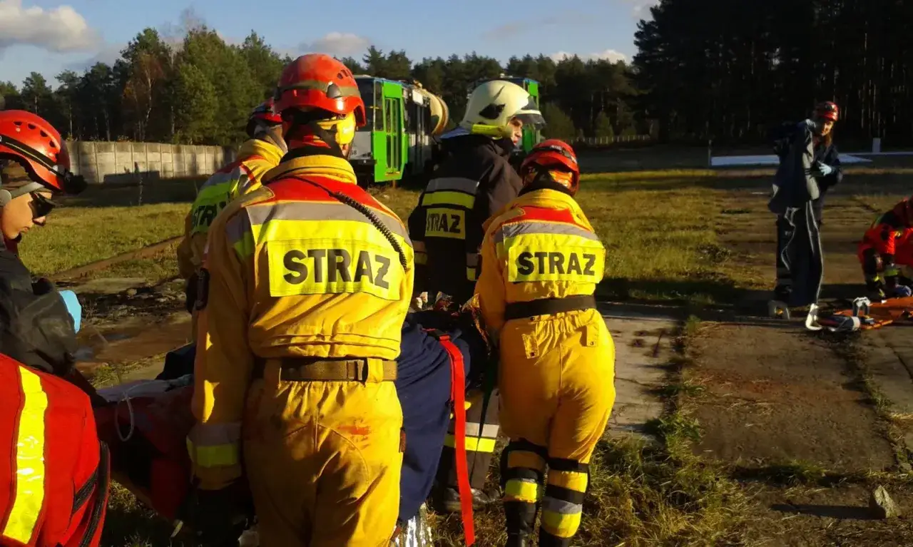 Strażacy z KSRG OSP w akcji, przygotowują się do transportu poszkodowanego. W tle przewrócony tramwaj.