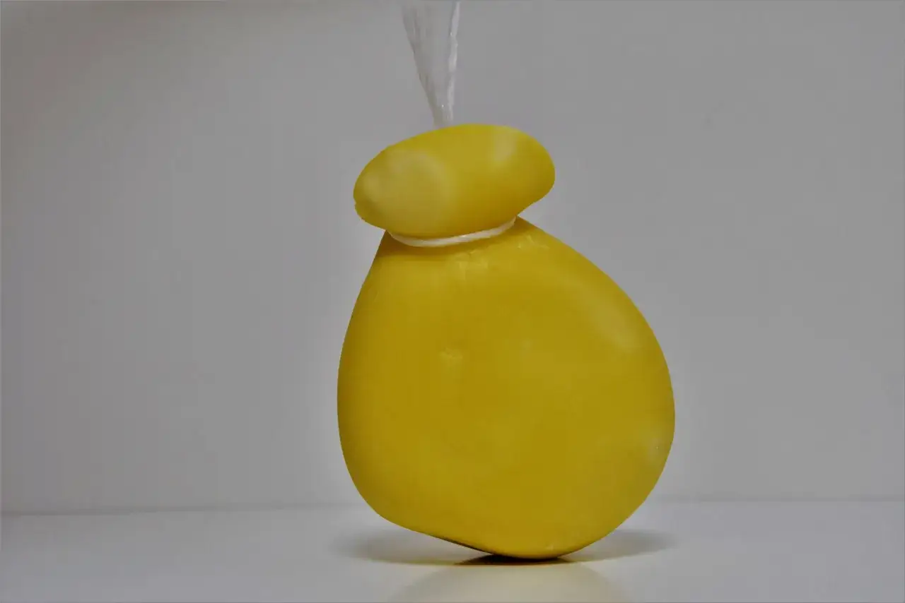 Formaggio giallo a forma di peretta, appeso per un filo bianco.