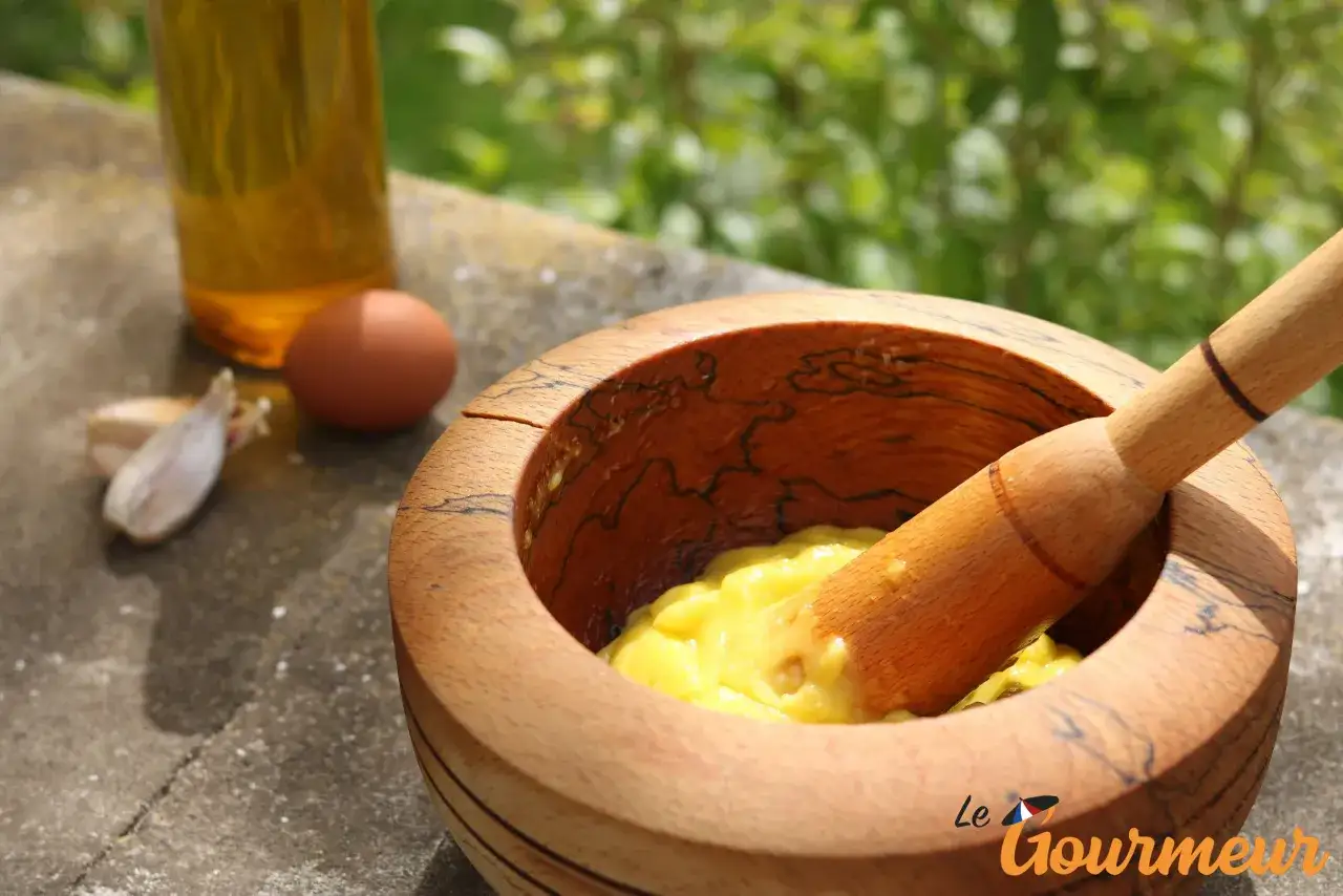 Préparation de la recette aïoli grand-mère : mortier en bois, œuf, ail et huile d'olive pour une sauce crémeuse.