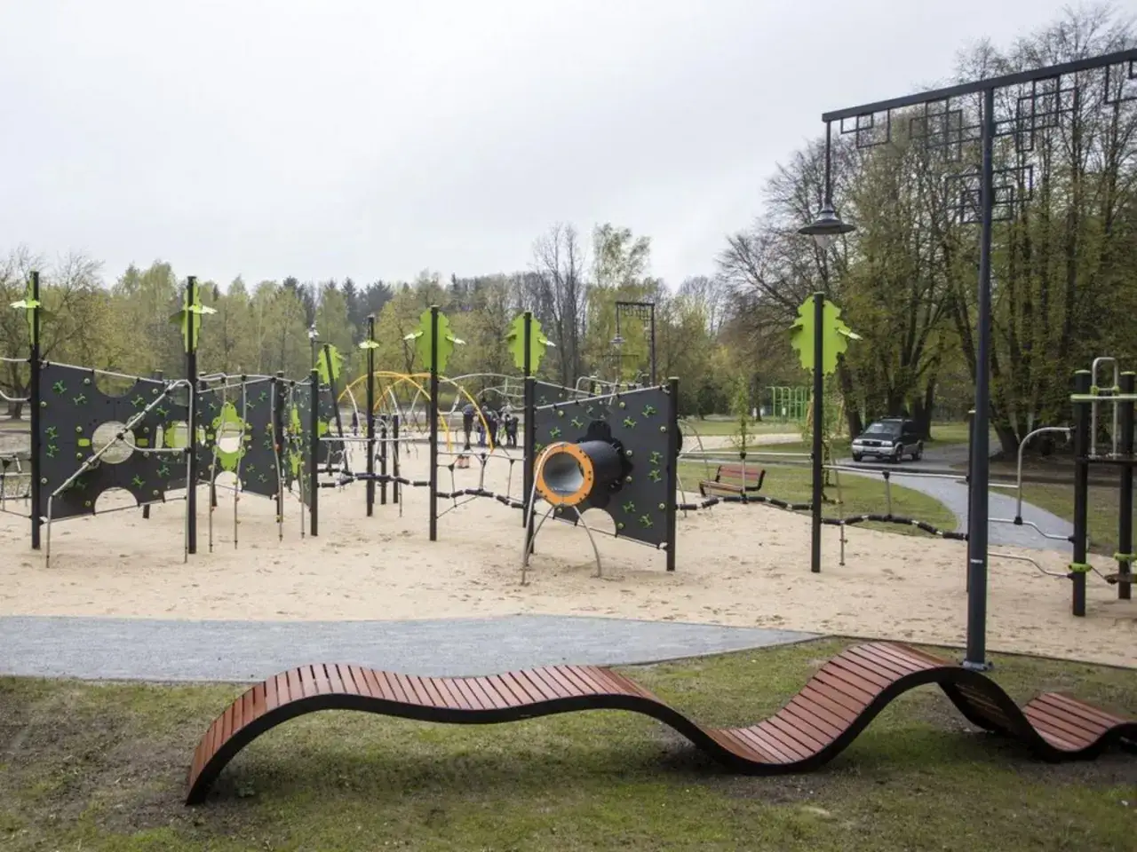 Nowoczesny plac zabaw w parku na zdrowiu z piaskownicą, ściankami wspinaczkowymi i nietypową ławką.
