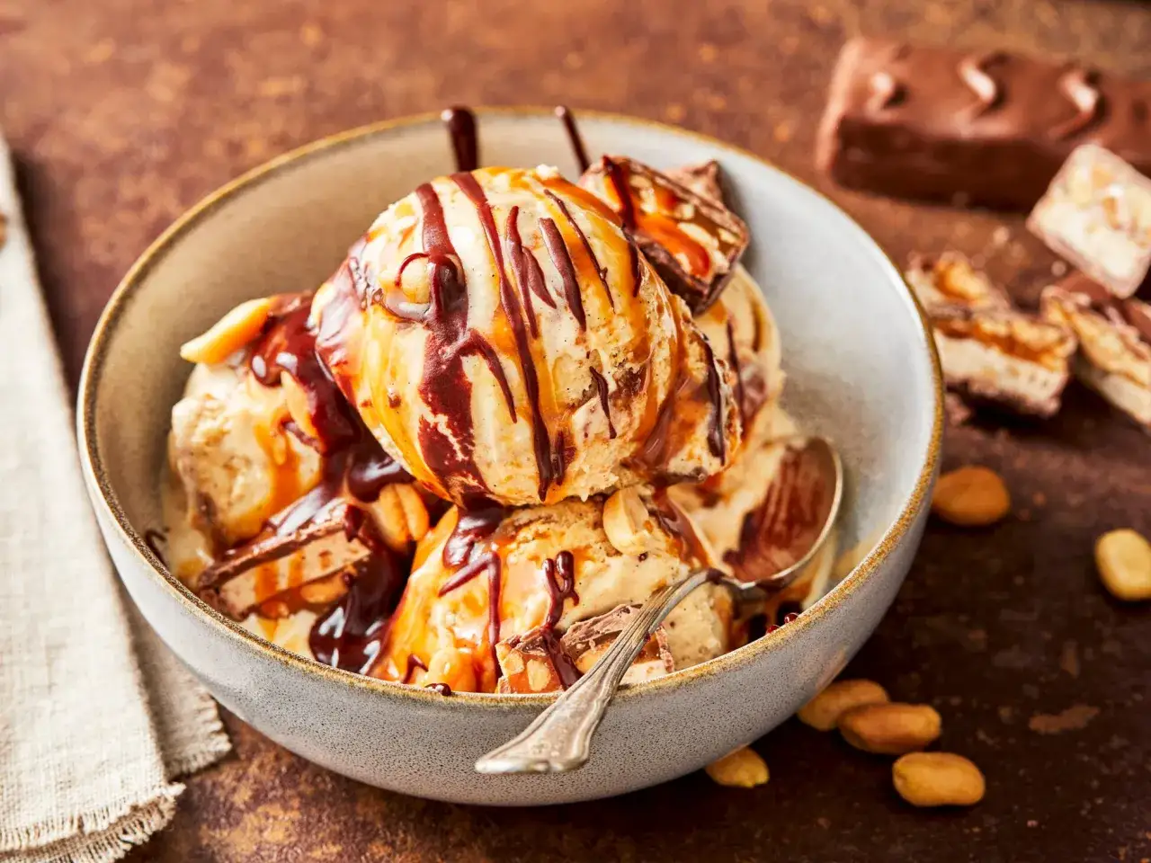 Schüssel mit Eiscreme, Karamell und Schokoladensauce, garniert mit Snickers-Stücken. Perfekt, wenn du Snickers Eis selber machen möchtest!