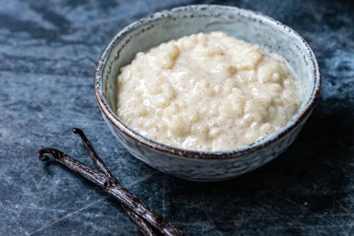 Un bol de riz au lait crémeux, parsemé de points de vanille, à côté de gousses de vanille. Une invitation à découvrir une recette de riz au lait réconfortante.