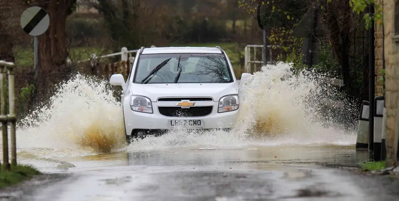 Biały Chevrolet z impetem wjeżdża w głęboką kałużę, powodując potężny aquaplaning i rozbryzgując wodę na boki.