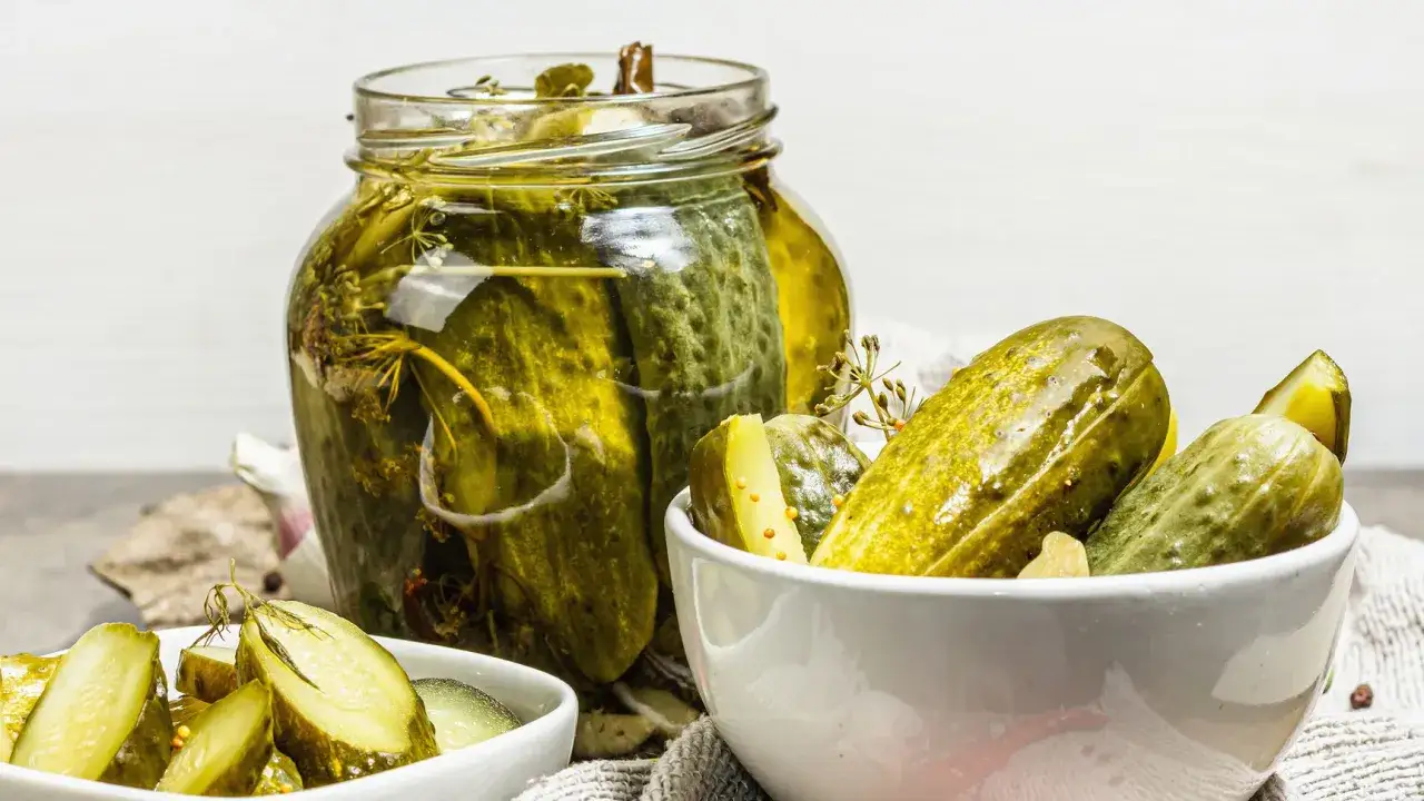 Vaso di vetro e ciotole piene di cetriolini in agrodolce, con aneto e spezie.