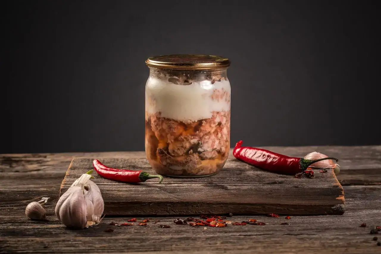 Słoik z przetworzonym mięsem mielonym, idealny do sosu do spaghetti. Obok papryczki chili i czosnek. Poznaj, jak pasteryzować sos do spaghetti z mięsem mielonym.