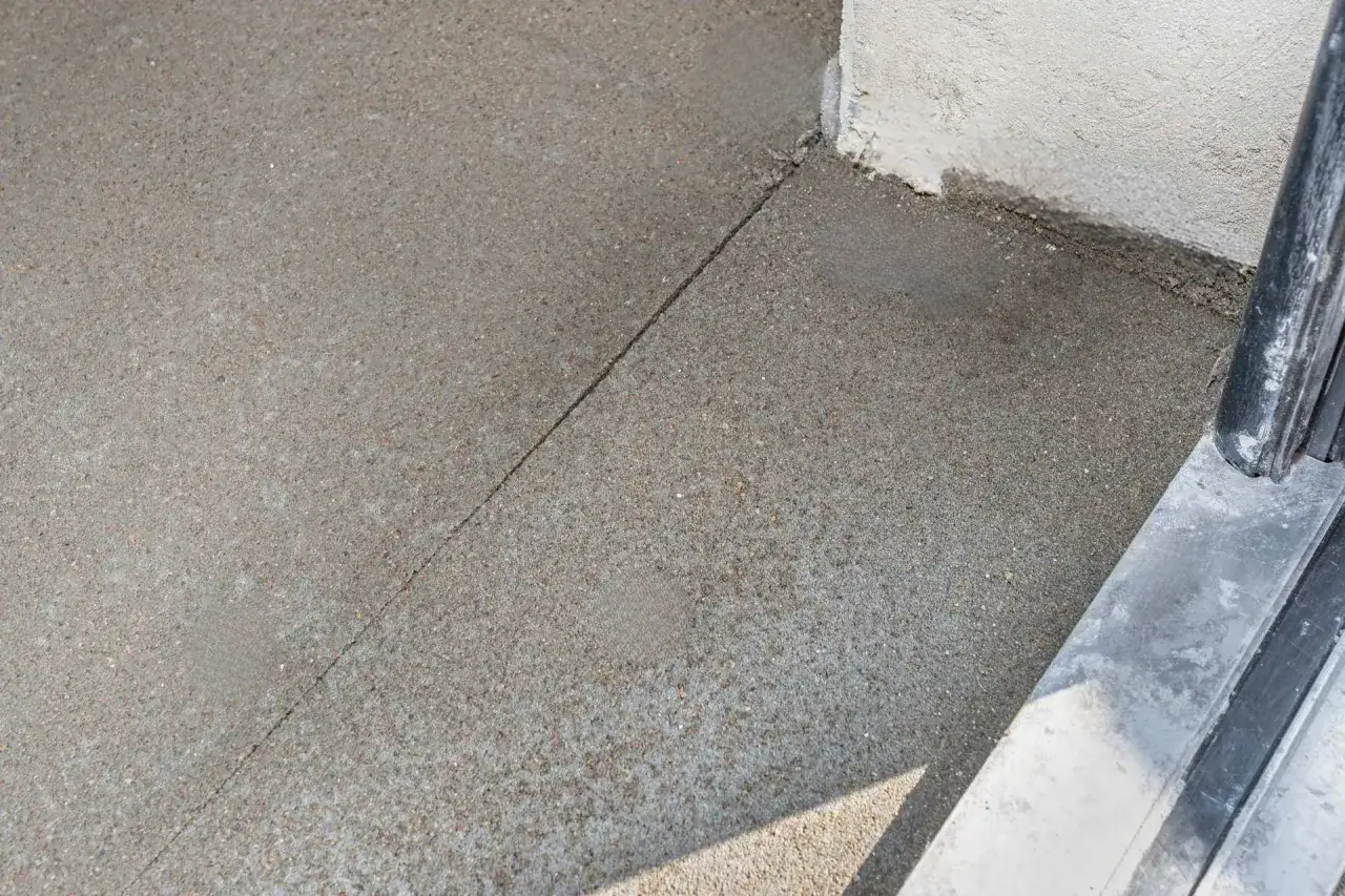 Świeżo wylany beton na podjazd, z widocznym podziałem i fragmentem ściany.