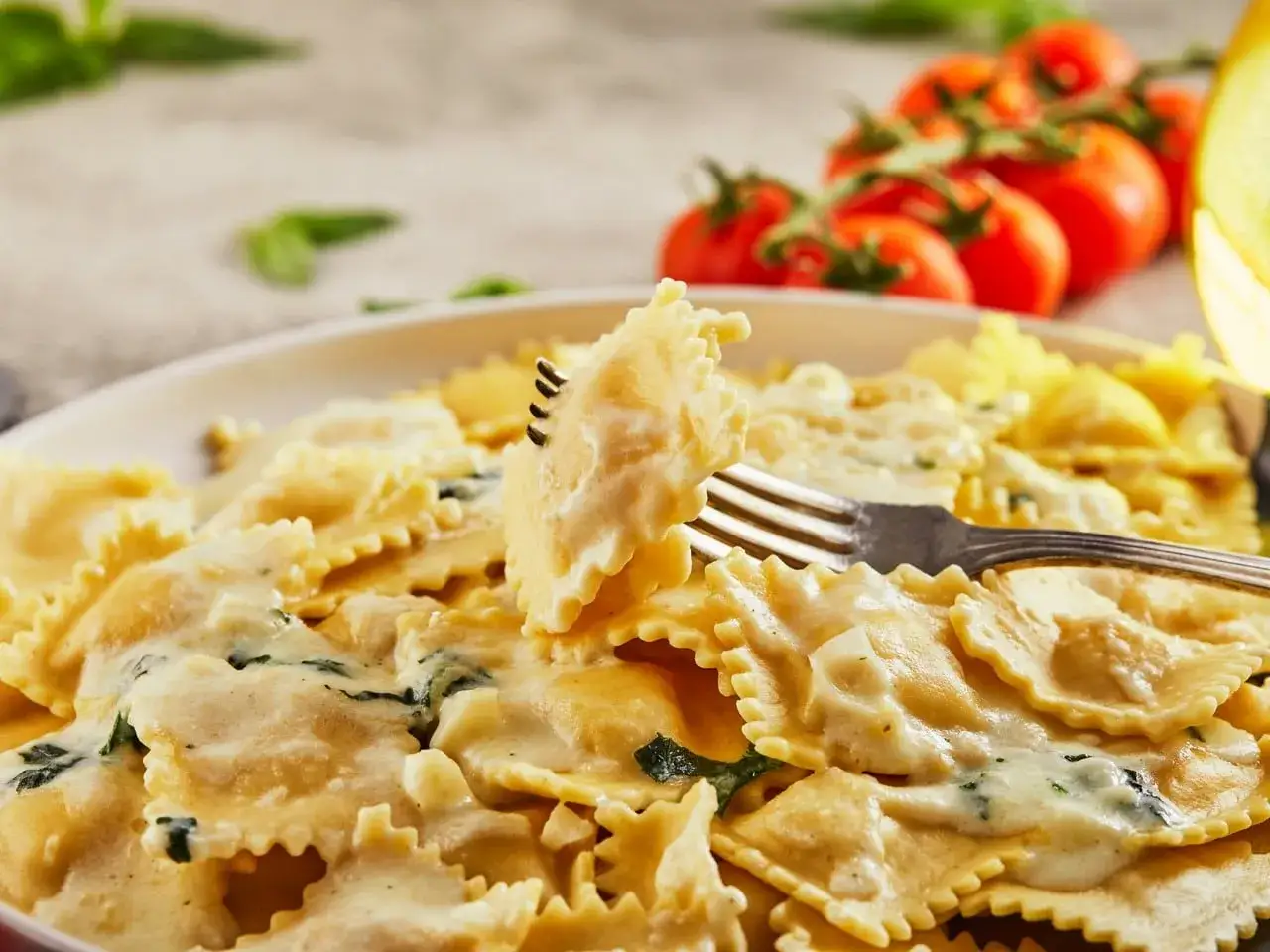 Raviolis cubiertos con una cremosa salsa ragu bianco, con tomates cherry y albahaca al fondo.