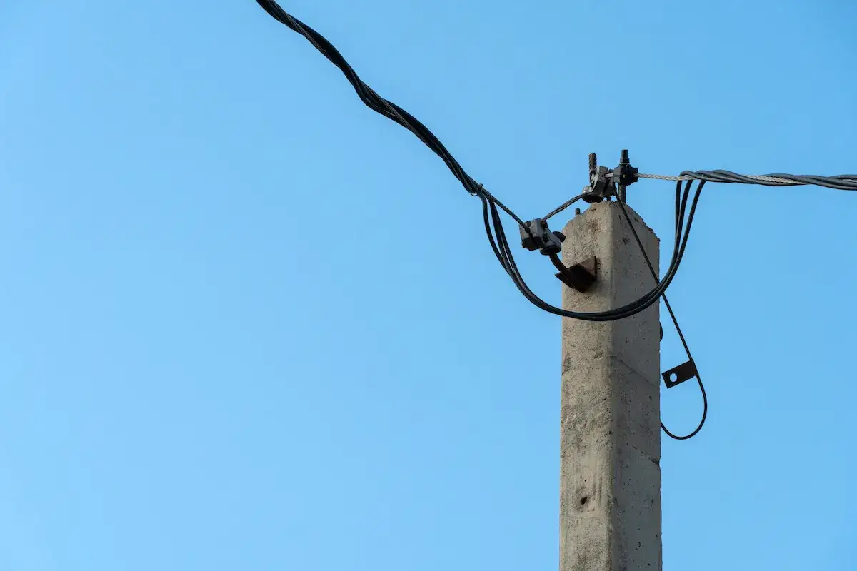 Betonowy słup niskiego napięcia z kablami elektrycznymi na tle błękitnego nieba.