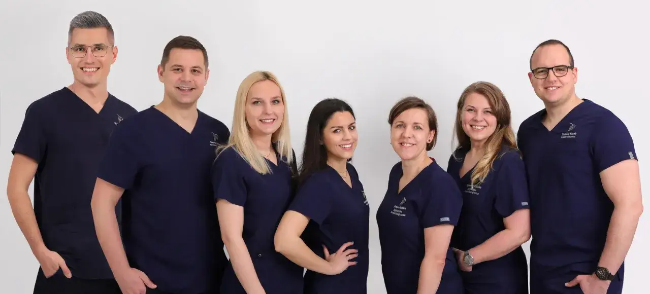 Grupa uśmiechniętych dentystów w granatowych uniformach na białym tle.