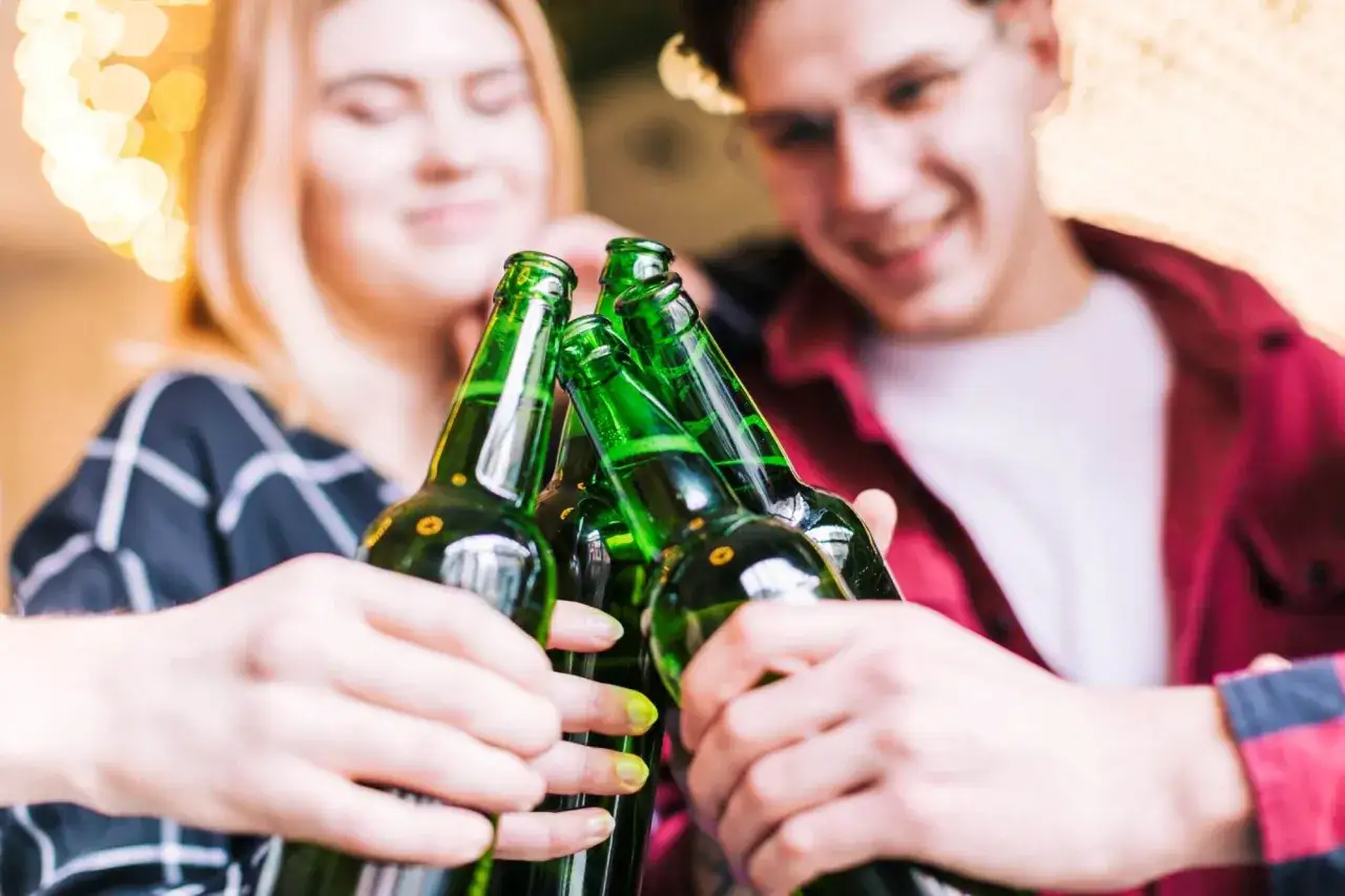 Młodzi ludzie wznoszą toast butelkami piwa. Pamiętaj, co grozi za picie alkoholu w wieku 17 lat.