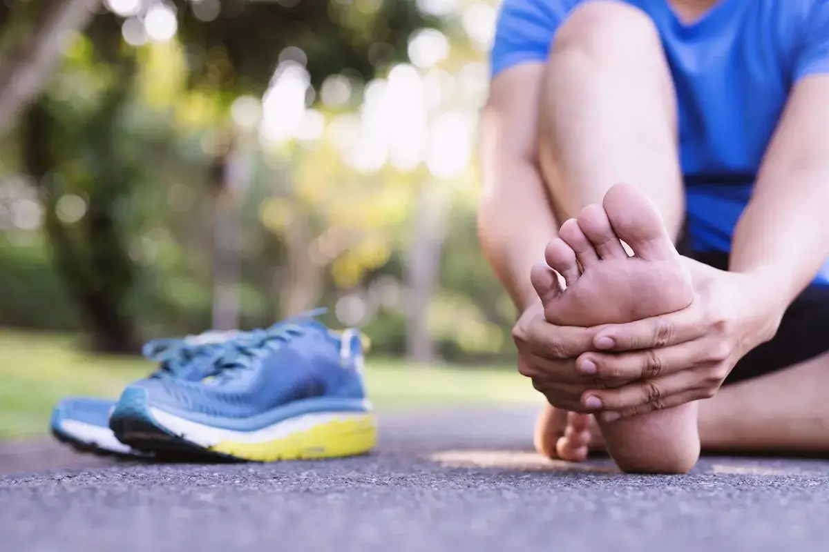 Ból stopy po treningu biegowym dla początkujących. Obok leżą niebieskie buty sportowe.