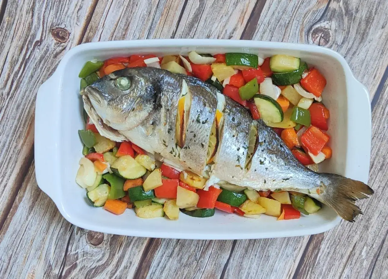 Dorada entera horneada con rodajas de limón y un surtido de verduras al horno: pimientos, calabacín y patatas.