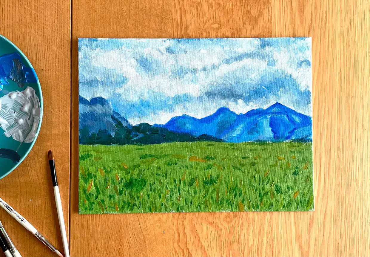 Peinture paysage facile débutant : un champ d'herbe verte sous un ciel bleu et nuageux, avec des montagnes bleues en arrière-plan.