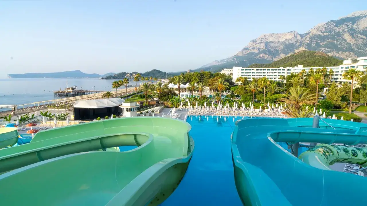 Zjeżdżalnie wodne w Mirage Park Resort, basen, plaża i góry w tle.