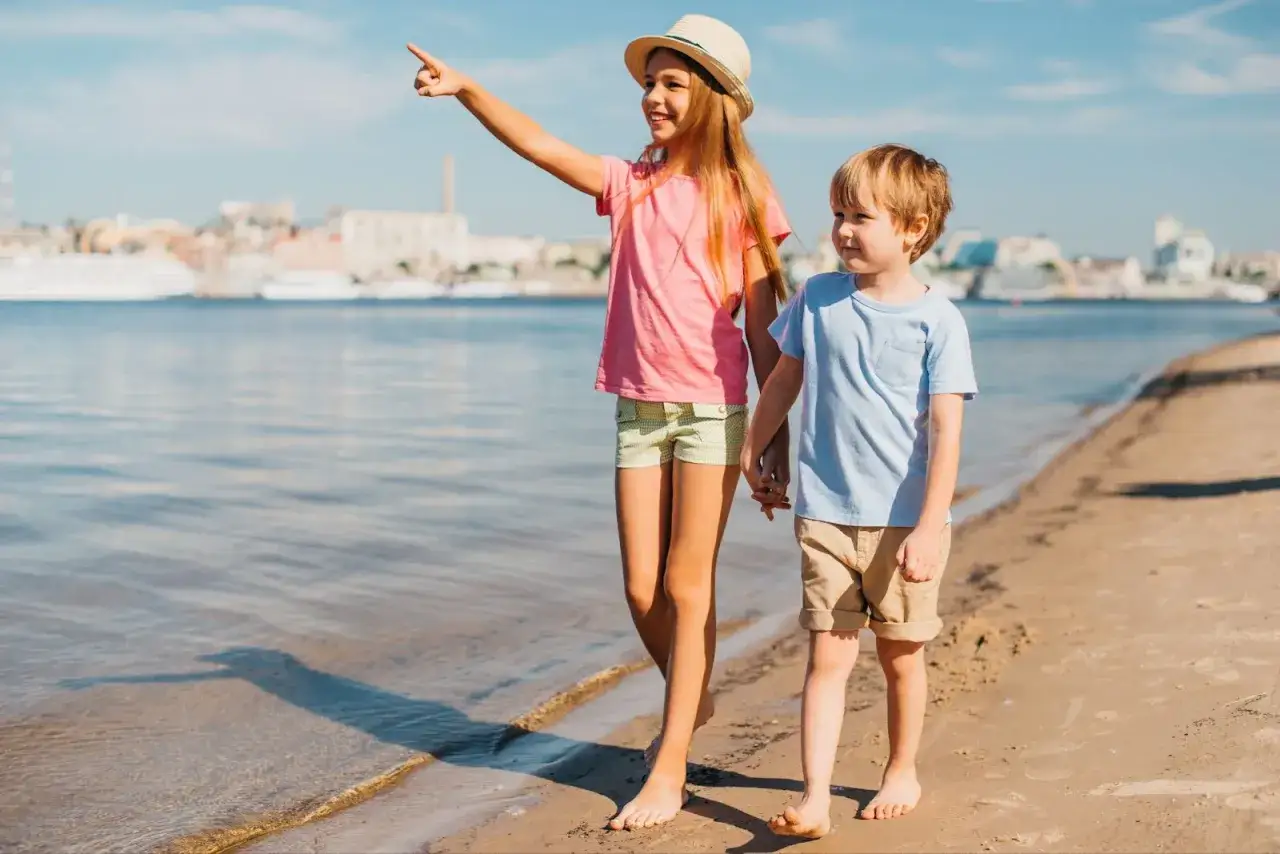 Dos niños pasean por la playa, la mayor señala algo en el horizonte. ¡Un día perfecto para disfrutar de Huelva con niños!