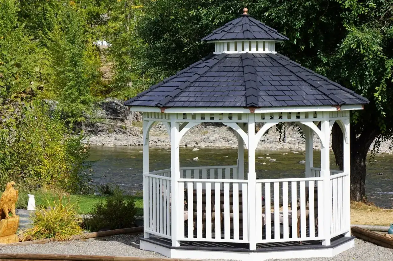 A white gazebo with a dark roof sits by a river, offering a peaceful spot. This image shows how to build a gazebo for a scenic retreat.
