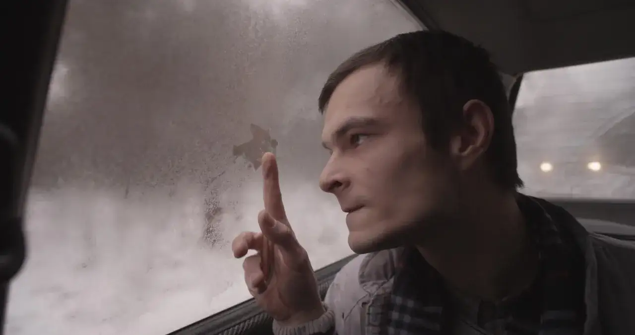Dawid Ogrodnik w filmach, zamyślony, rysuje palcem na zaparowanej szybie samochodu.